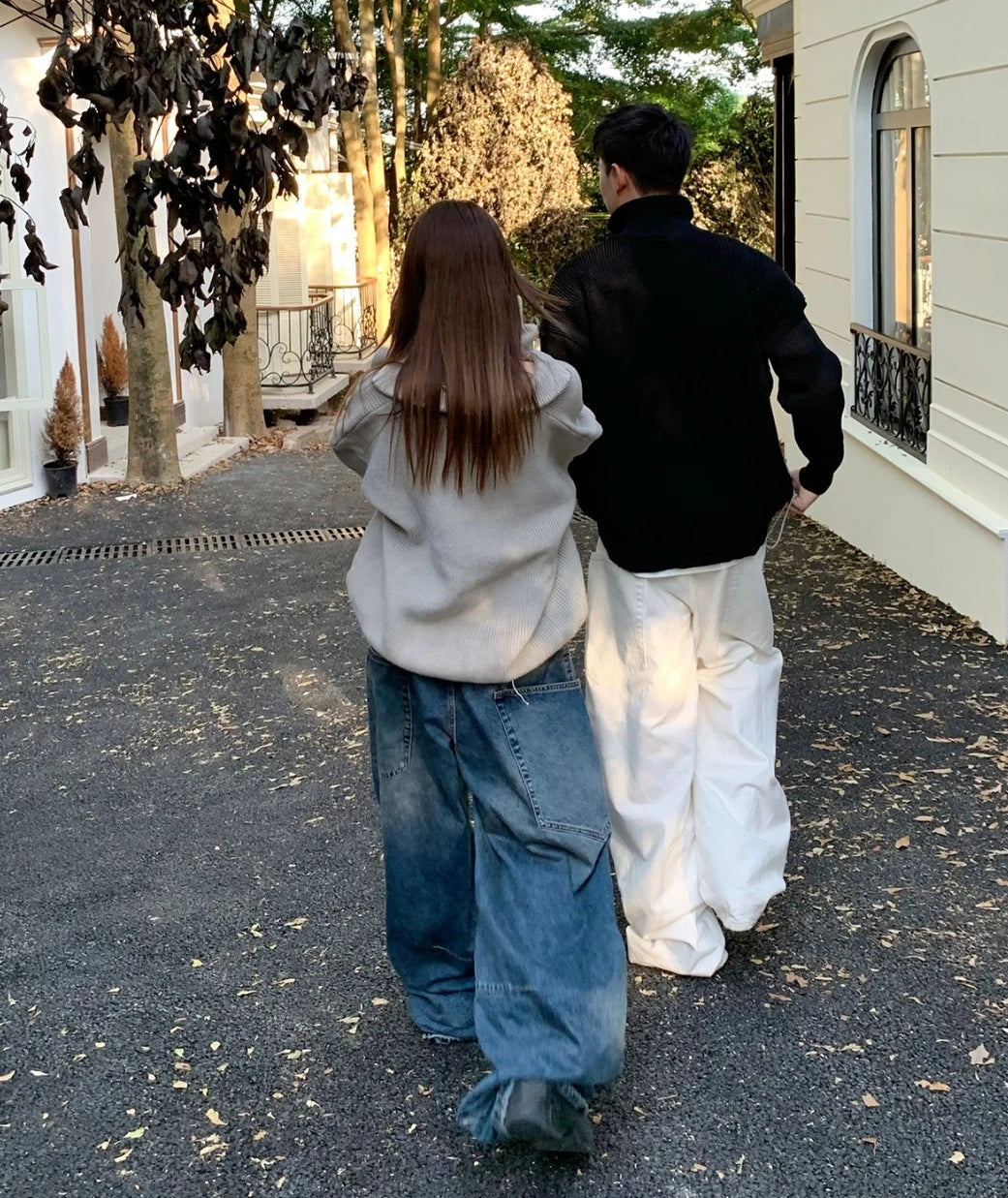 黒とグレーの英字ロゴジップアップニットを着たカップルの後ろ姿。屋外。