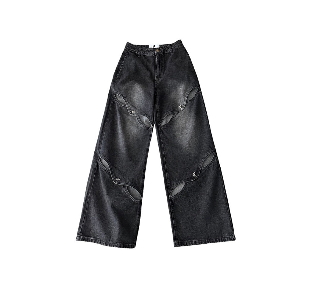 白背景に平置きしたブラックカットアウトワイドデニムパンツのフロント全体画像。脚部分に並ぶカットアウトスリットデザインがはっきり分かる。