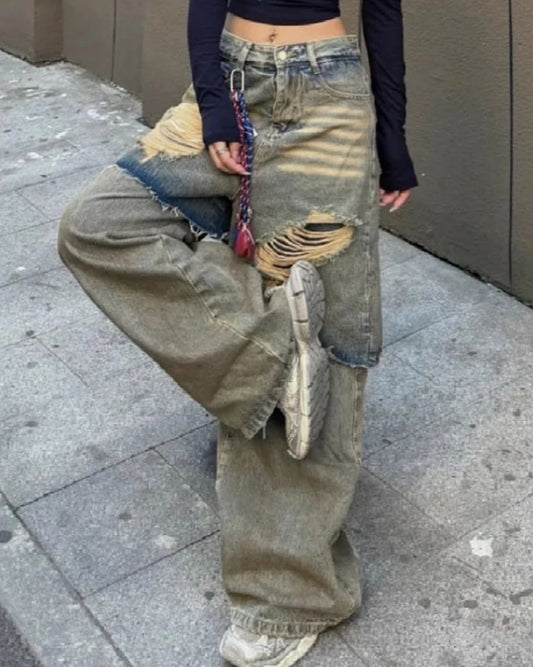 ダメージワイドデニムを着用し、片足を上げたポーズ。ストリート感のある色落ちとバギーシルエットが目立つ。