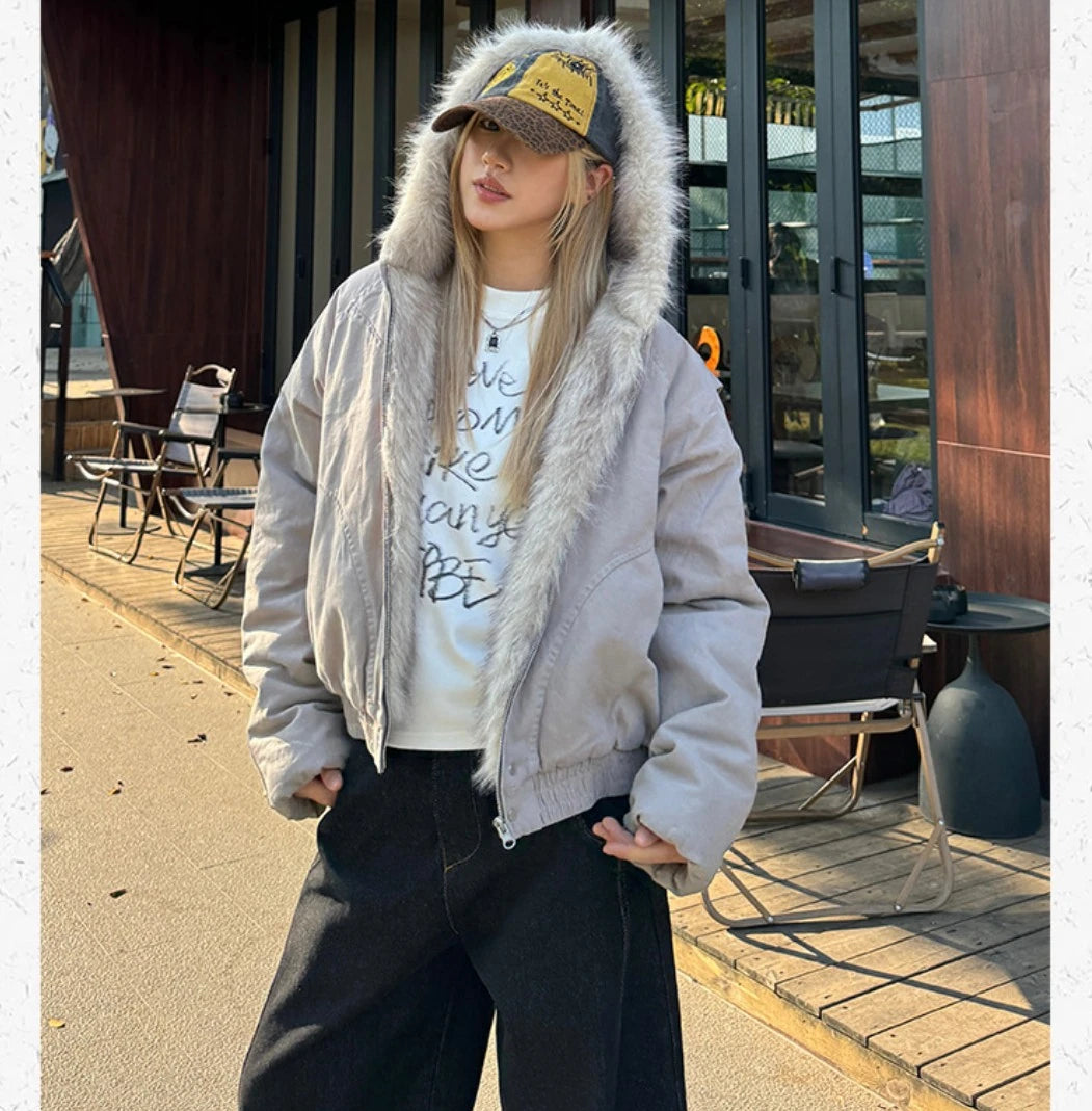 フードを被り、正面で立ちポーズをとる女性の全身ショット。カフェテラスの前で撮影。