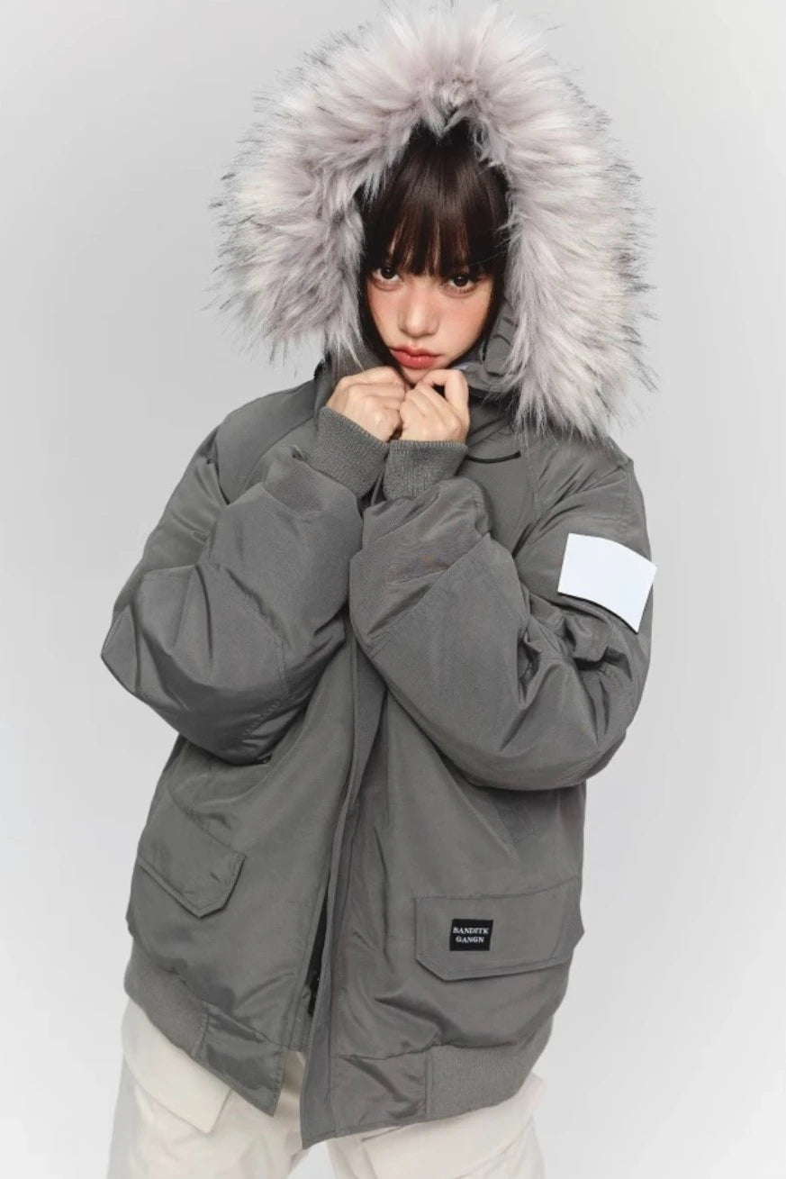 グレーのファー付きダウンジャケットを着たモデル。襟元に手を添えており、袖のワッペンが確認できる。