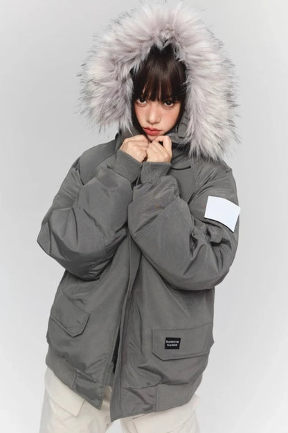 グレーのファー付きダウンジャケットを着たモデル。襟元に手を添えており、袖のワッペンが確認できる。