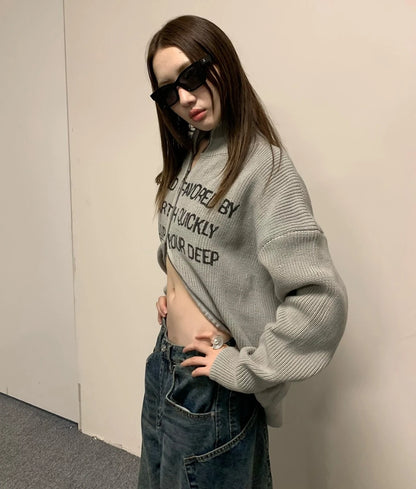 グレーの英字ロゴジップアップニットをへそ出しで着た女性モデル。サングラス。