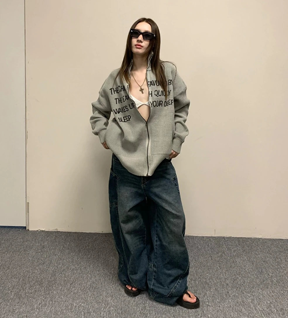 グレーの英字ロゴジップアップニットとワイドデニムの全身コーデ。サングラス。