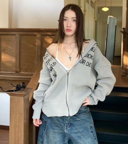 グレーの英字ロゴジップアップニットを着た女性モデル。階段での全身ショット。