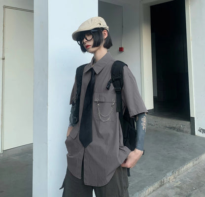 グレーのネクタイ付きシャツを着たモデル。キャスケット着用。ポケットに手を入れ、少し斜めに立つ。