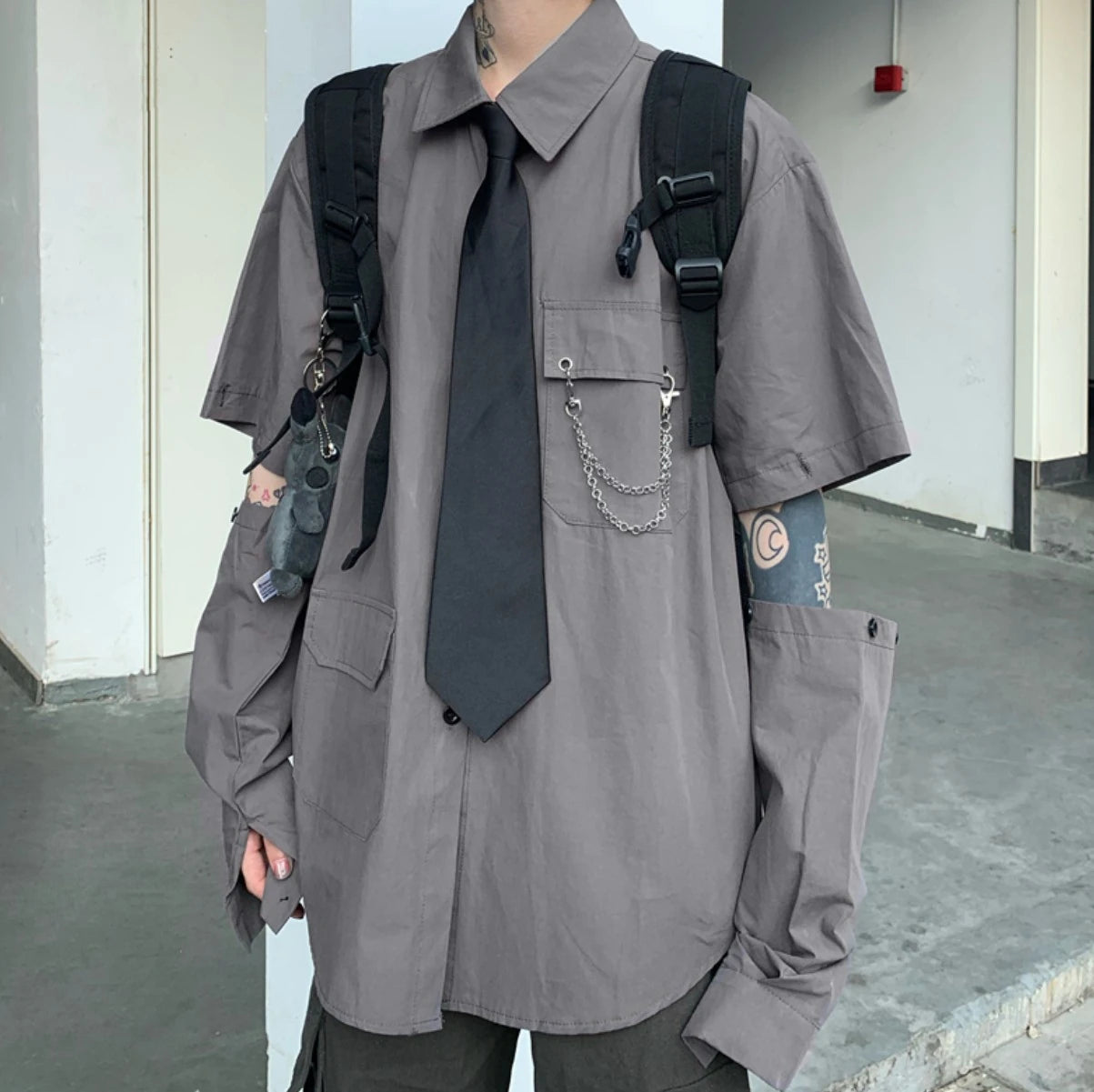 グレーのネクタイ付きシャツを着たモデル。袖のボタンを外し、腕をのぞかせた着こなし。正面立ち姿。