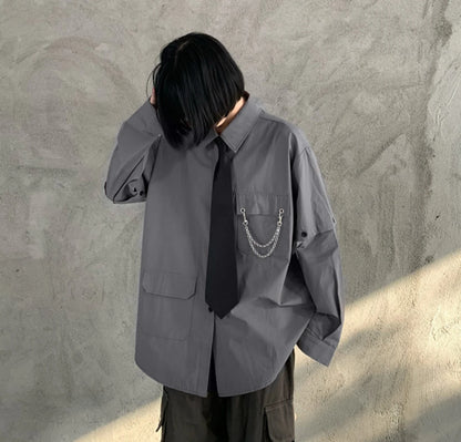 グレーのネクタイ付きシャツを着たモデル。うつむいて髪に手を添えるポーズ。胸元のチェーン装飾。