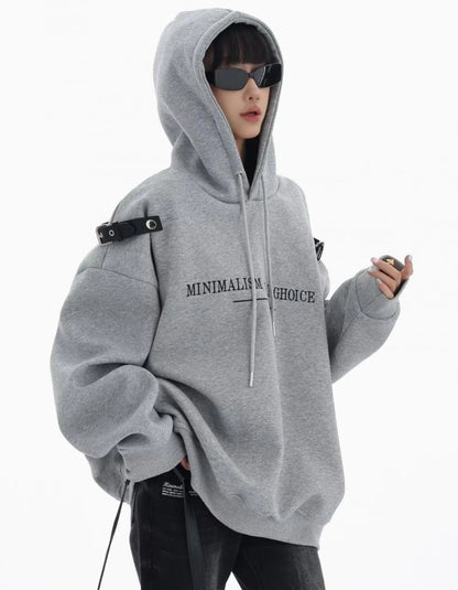 グレーのショルダーベルト付きオーバーサイズパーカーのフードをかぶった横向きコーデ。袖にボリュームのあるラフなストリートスタイル。