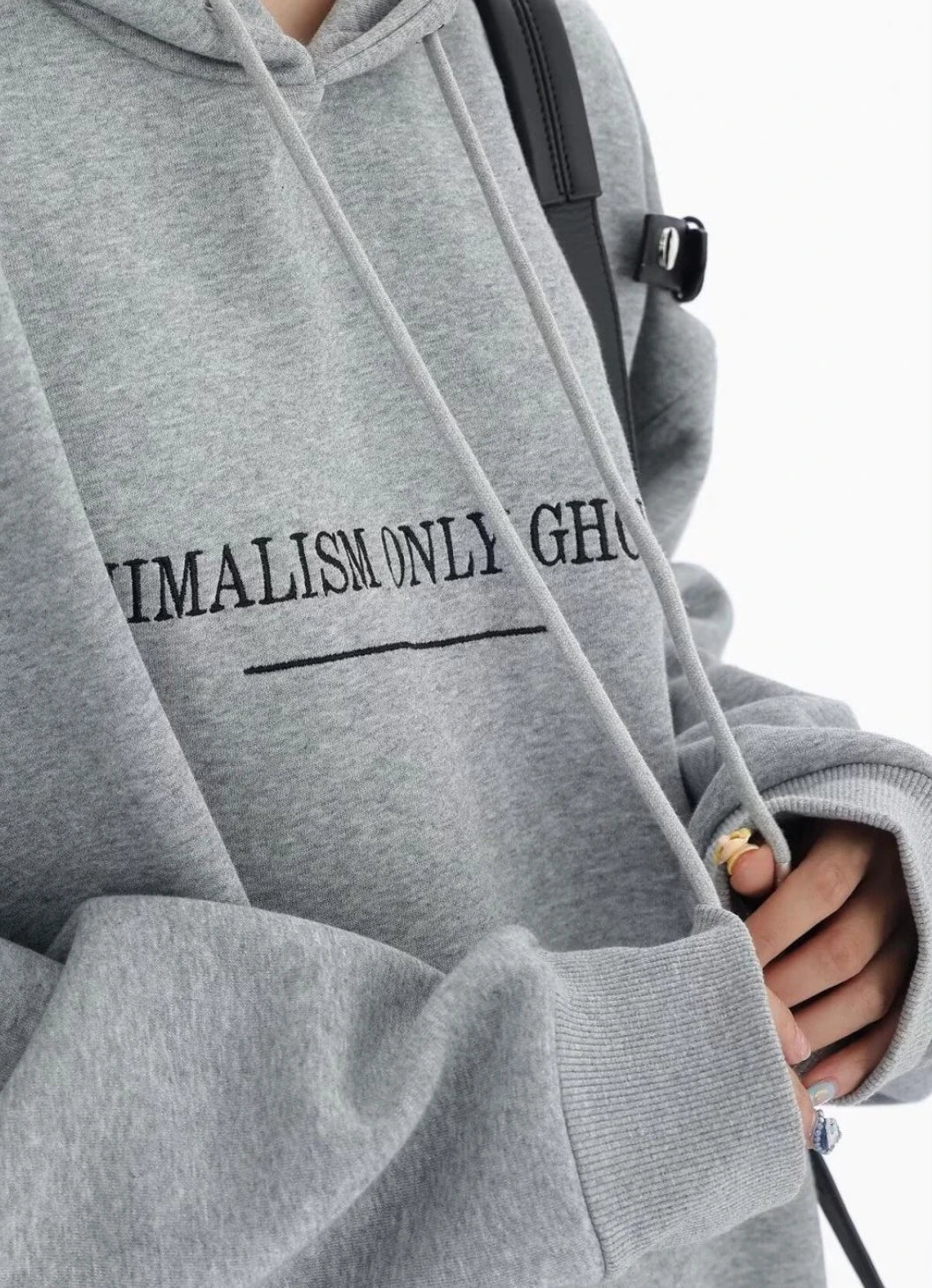 グレーのショルダーベルト付きオーバーサイズパーカーの胸元ロゴとフード紐のディテールアップ。袖口リブと生地感が分かるクローズアップ。