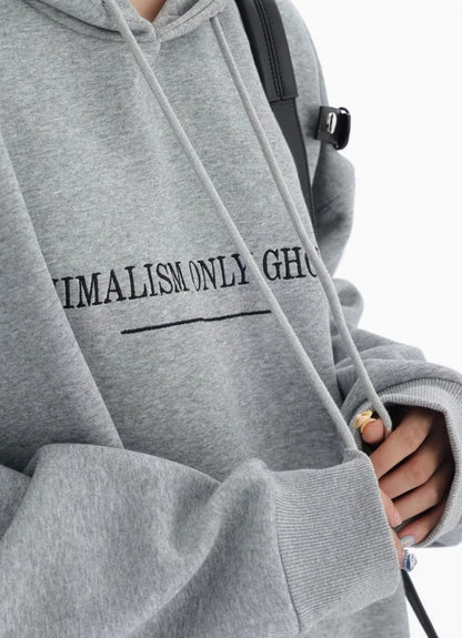 グレーのショルダーベルト付きオーバーサイズパーカーの胸元ロゴとフード紐のディテールアップ。袖口リブと生地感が分かるクローズアップ。