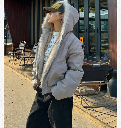 ファー付きフードブルゾンとキャップを着用し、外のテラス席で横向きに立つ女性。