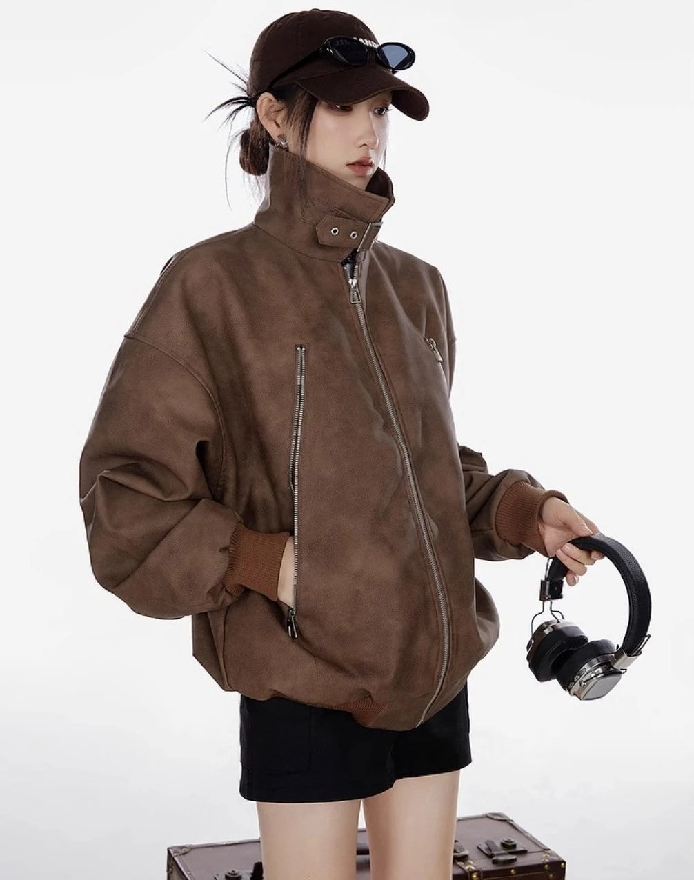 ブラウンのスタンドカラージャケットを着た女性がヘッドホンを持つ横向き写真