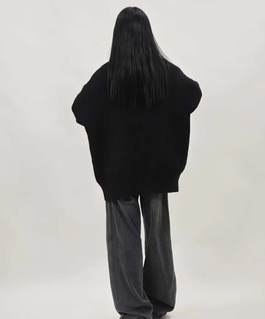 ブラックのオーバーサイズジップニットカーディガンを着たレディースモデルの後ろ姿とドロップショルダーのゆったりシルエット