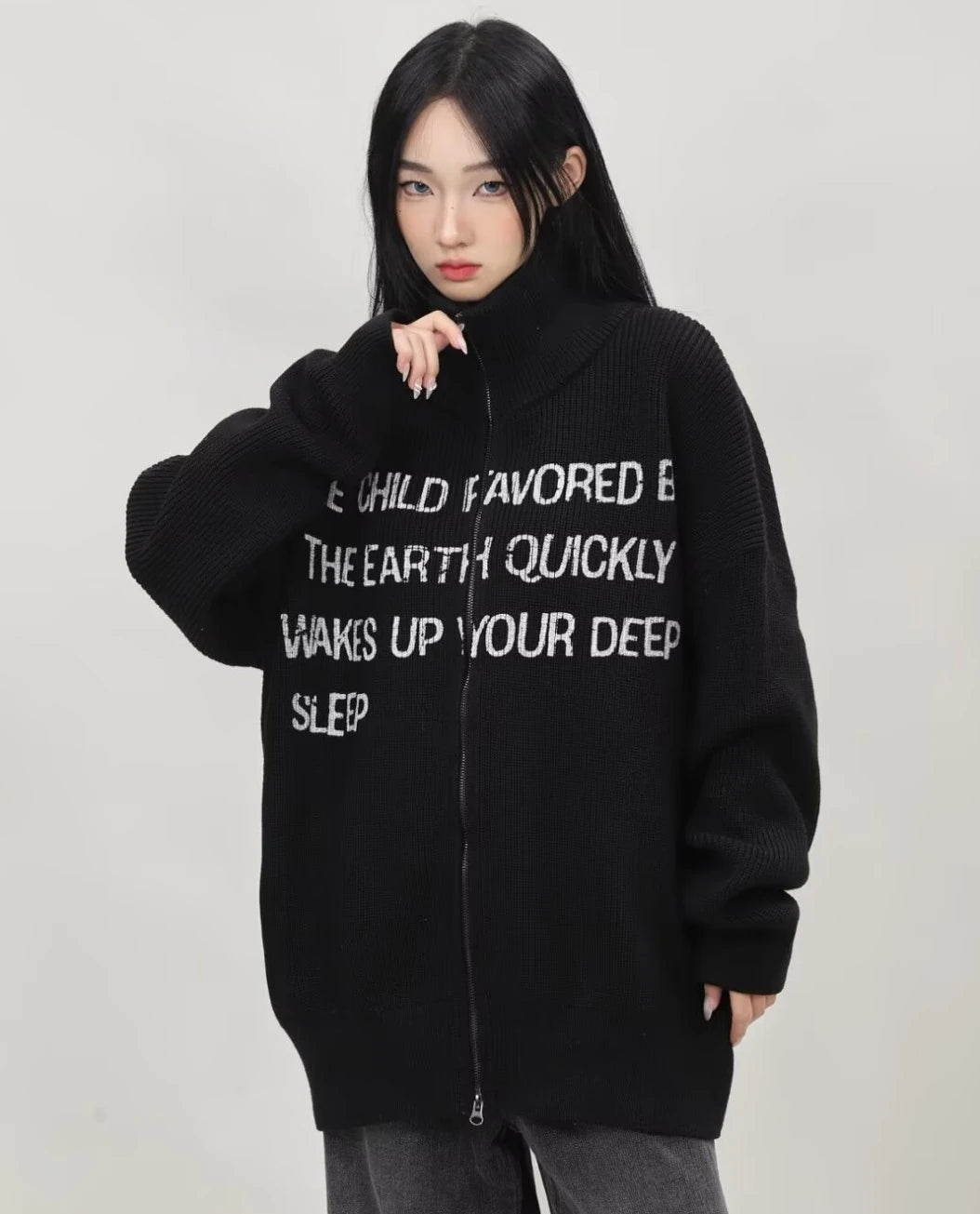 ブラックの英字メッセージジップニットカーディガンを首元まで閉め、胸元のロゴデザインを強調したレディースモデルの上半身アップ