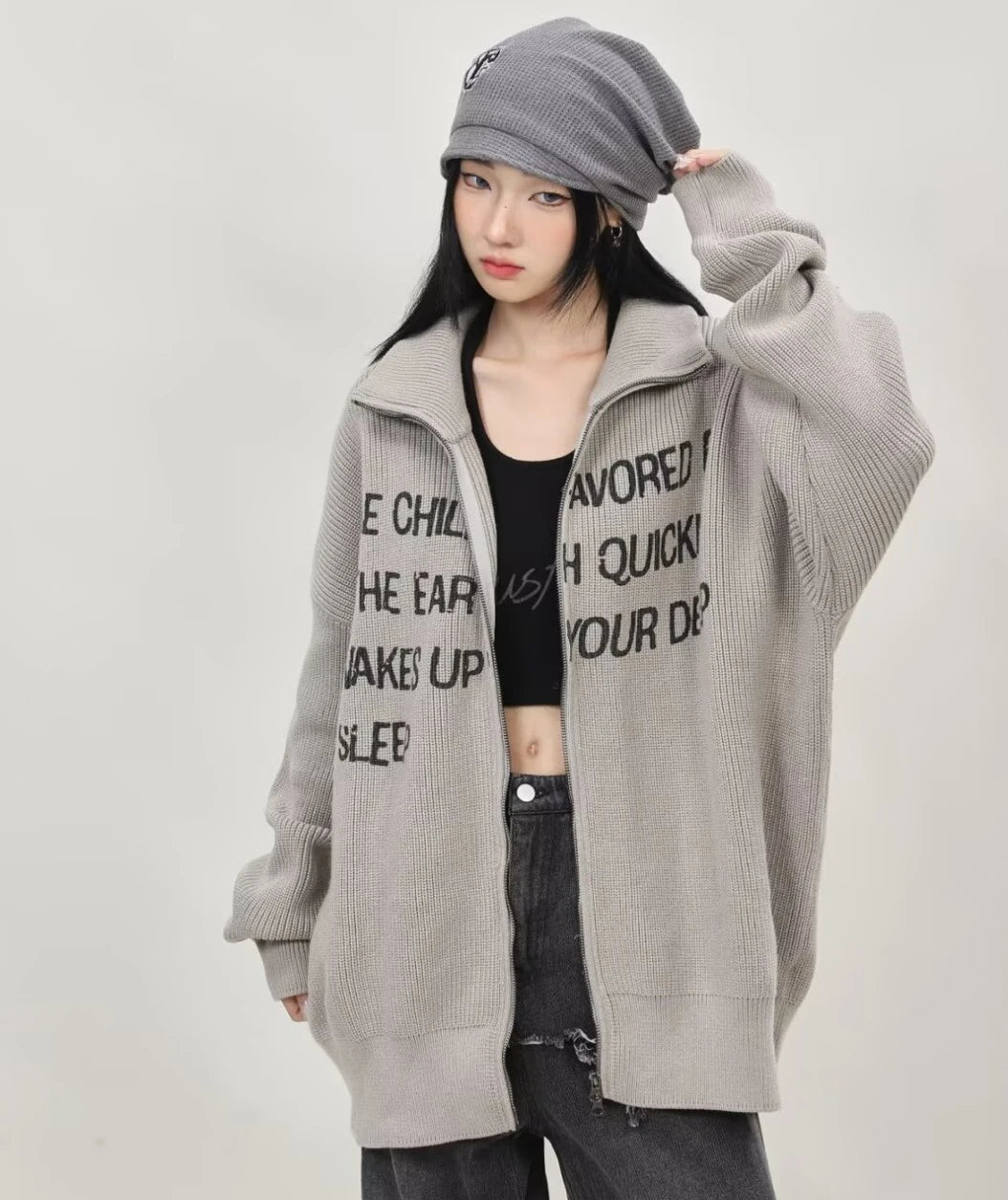 グレーの英字メッセージジップニットカーディガンを前開きで羽織り、ビーニーとワイドデニムを合わせたレディースコーデの正面全身