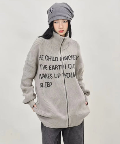 グレーの英字メッセージジップニットカーディガンをフルジップで閉め、ポケットに手を入れたレディースモデルの正面ショット