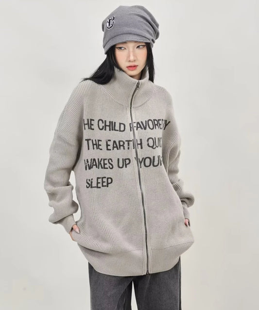 グレーの英字メッセージジップニットカーディガンをフルジップで閉め、ポケットに手を入れたレディースモデルの正面ショット