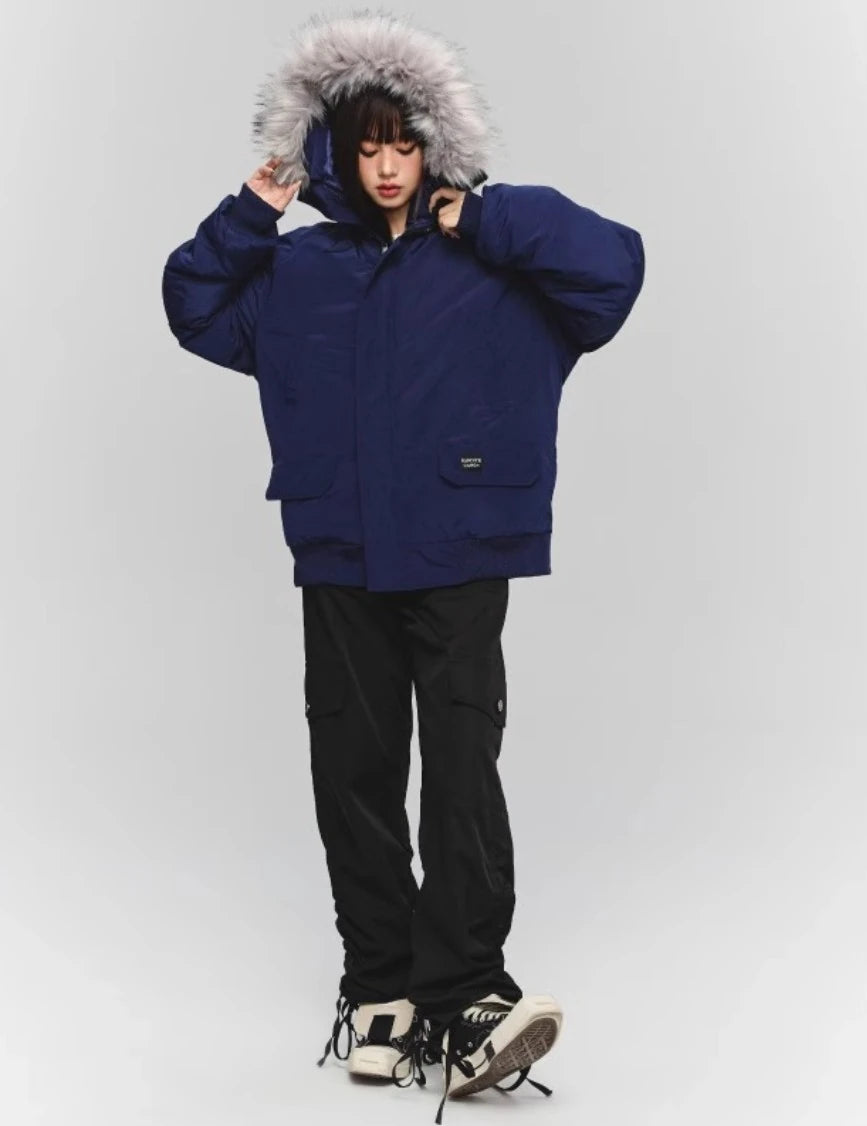 ネイビーのダウンジャケットと黒いパンツを着用したモデル。フードに手を添え、正面を見ている全身像。