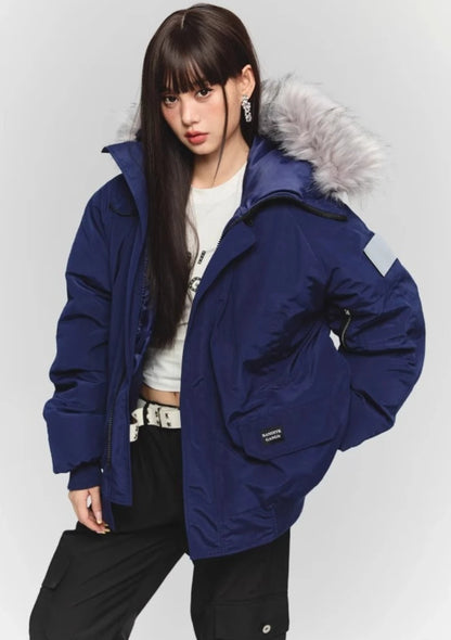 ネイビーのダウンジャケットを半開し、白いクロップドTシャツと黒いパンツを合わせたモデル。