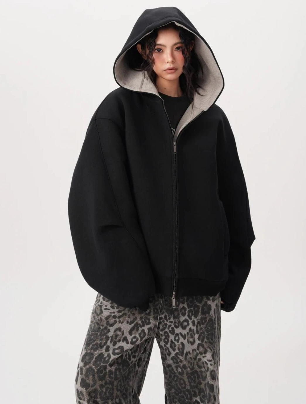 フードをかぶったモデルが裏地グレーのブラックオーバーサイズジップパーカーを着用しているバストアップ写真