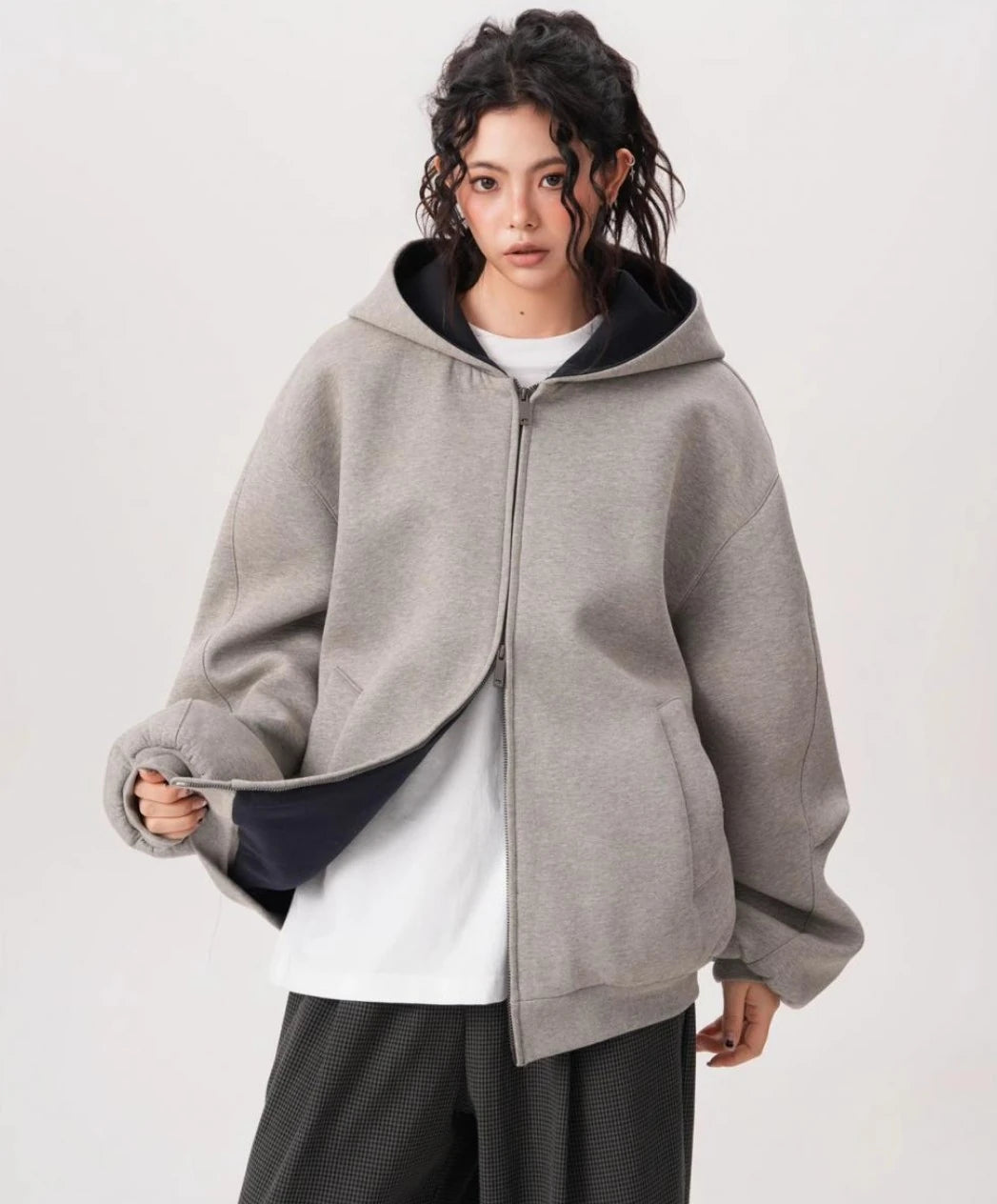 裾を軽くつまみ裏地を見せたグレーオーバーサイズジップパーカーのディテールとシルエットがわかる写真