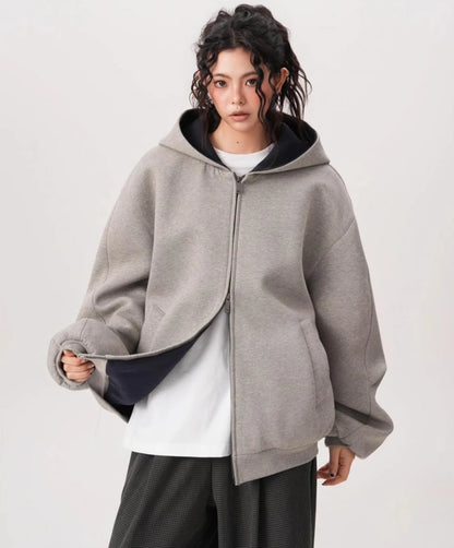 裾を軽くつまみ裏地を見せたグレーオーバーサイズジップパーカーのディテールとシルエットがわかる写真