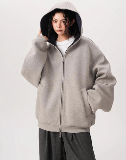 フードを深くかぶったモデルがグレーのオーバーサイズジップパーカーを前ファスナー閉めで着用している写真