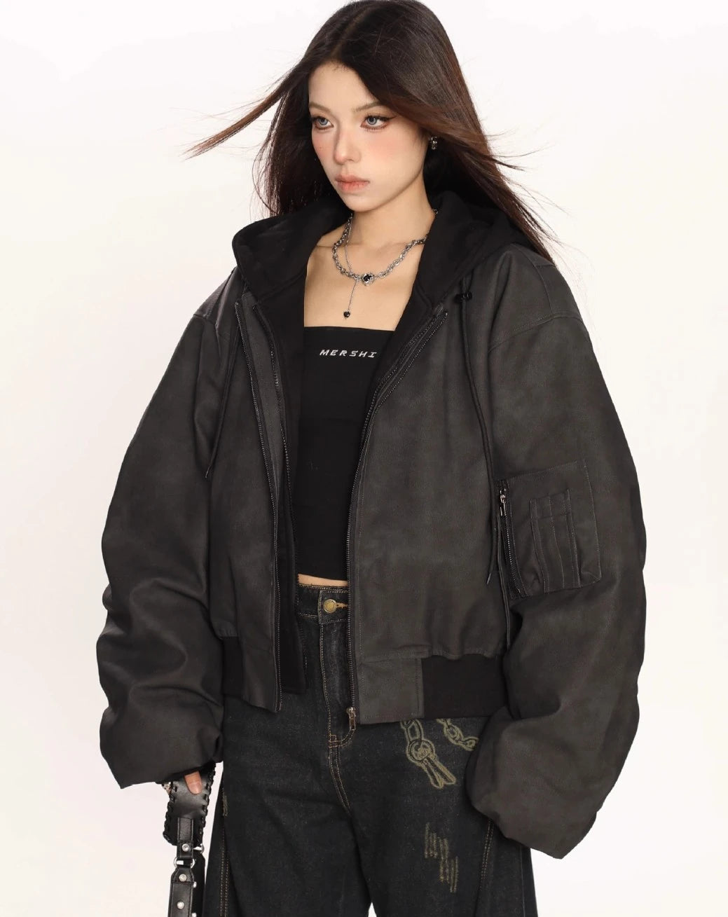 ブラックのオーバーサイズボンバージャケットを羽織り、斜め向きで片手にバッグのストラップを持ったモデルのウエストアップ