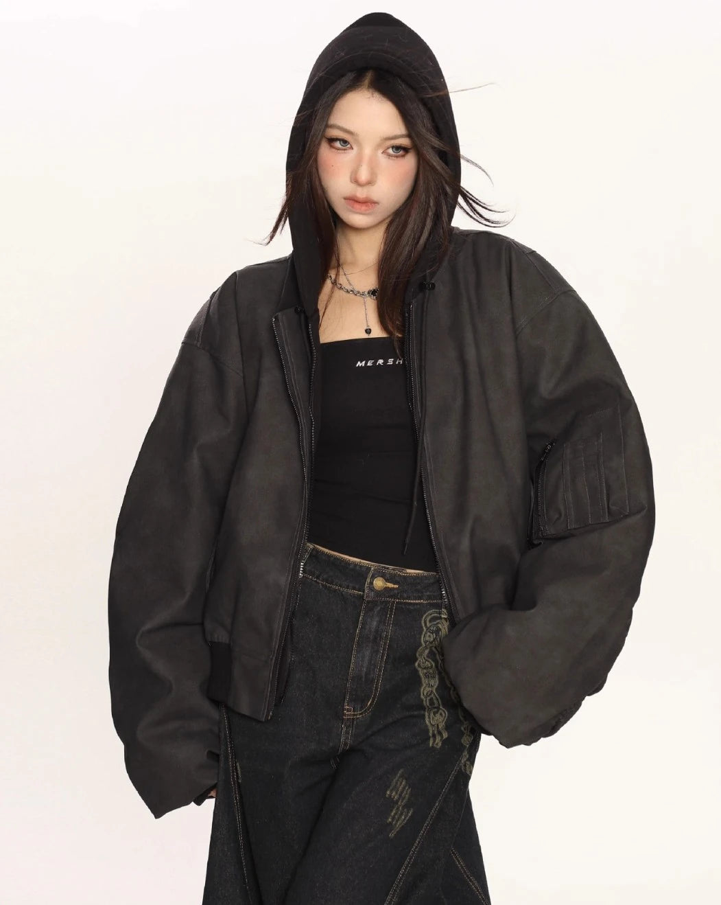 ブラックのオーバーサイズボンバージャケットのフードをかぶり、黒インナーとワイドデニムを合わせたモデルの上半身ショット