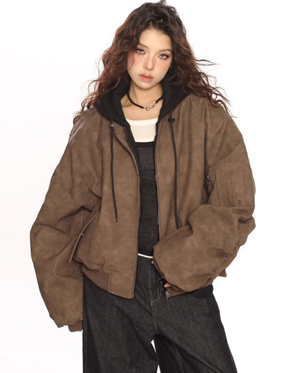 ブラウンのオーバーサイズボンバージャケットの前を少し開け、白インナーと黒トップスをレイヤードしたモデルのウエストアップ