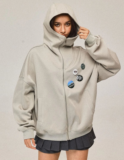 ライトベージュのジップパーカーのフードを深く被ったポーズ。ハイネックのデザインとゆったりとしたシルエット。