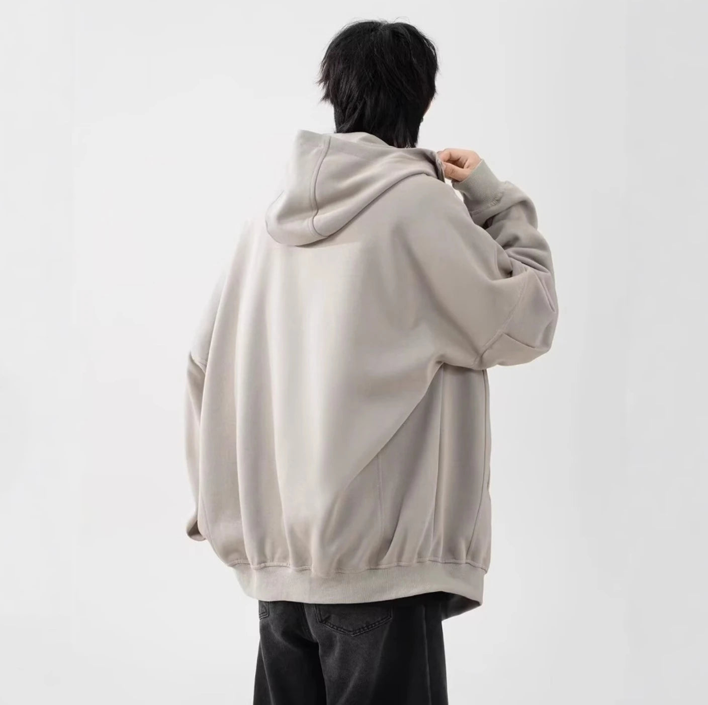 ライトベージュのパーカーを着用した男性モデルの後ろ姿。背中のドレープ感とシンプルなデザイン。