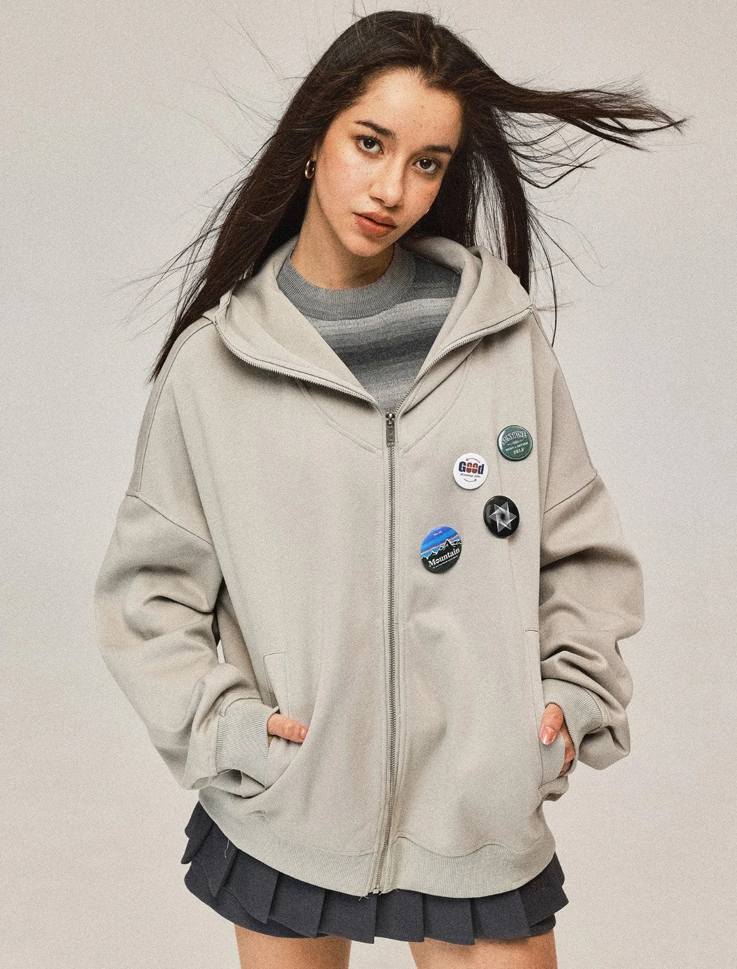 風になびく髪とライトベージュのパーカー。フードを下ろしたスタイルで、リラックスした雰囲気。