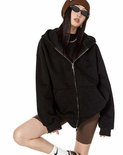 ブラックのオーバーサイズジップパーカーにブラウンのバイカーショーツを合わせ、片膝をついてポーズをとるモデルのコーデ