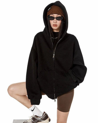 ブラックのオーバーサイズジップパーカーのフードをかぶり、片脚を台に乗せてポーズをとるモデルの正面ショット