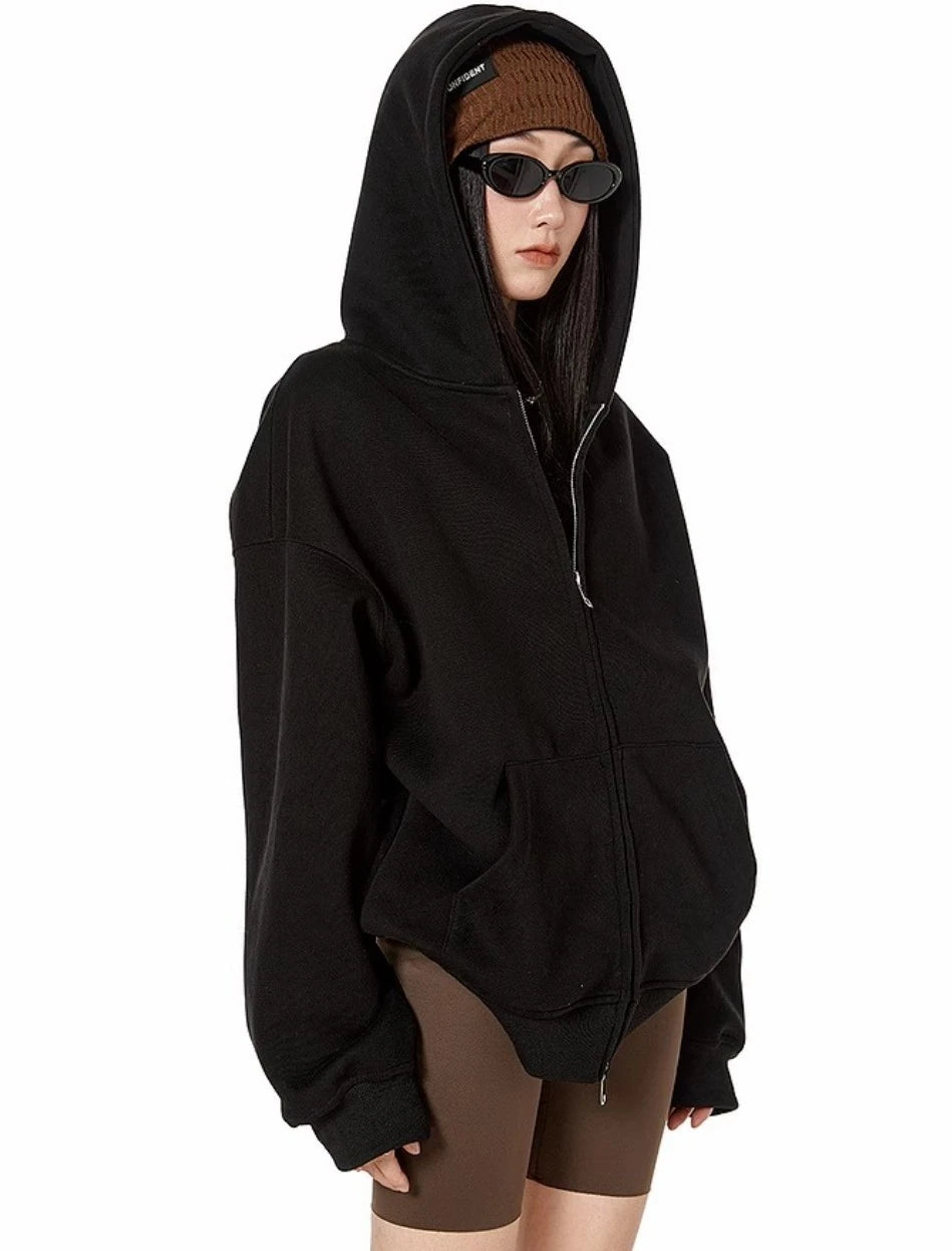 ブラックのオーバーサイズジップパーカーのフードをかぶり、ブラウンのバイカーショーツと合わせたモデルのサイドショット