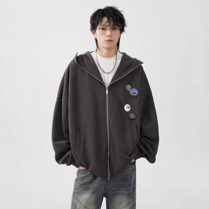 ダークブラウンのオーバーサイズジップパーカーを着用した男性モデルの正面写真。メガネと複数の缶バッジが特徴。