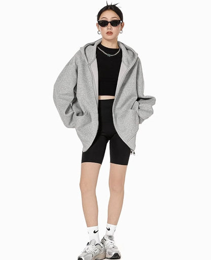 グレーのオーバーサイズジップパーカーを前開きで羽織り、ブラックのクロップドトップとバイカーショーツを合わせたモデルの全身コーデ