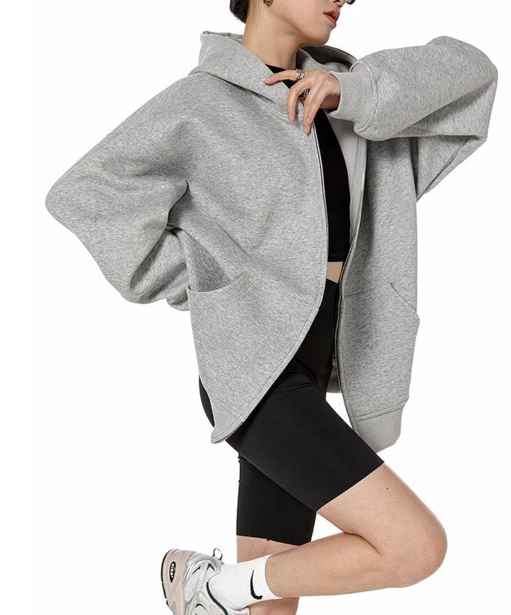 グレーのオーバーサイズジップパーカーを前開きで羽織り、片脚を曲げてポーズをとるモデルのサイド全身ショット