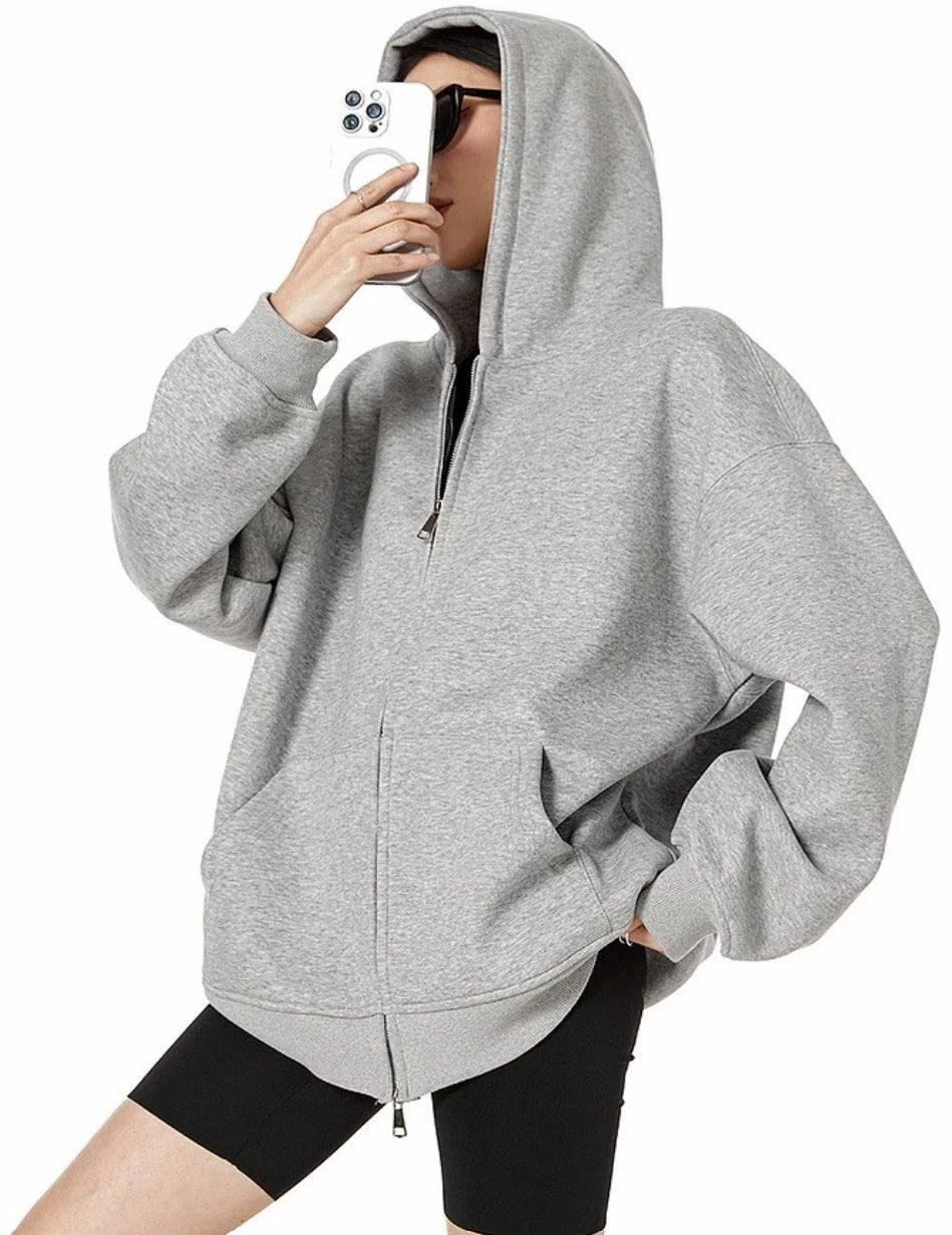 フードをかぶったグレーのオーバーサイズジップパーカーを着て、横向きでスマホを顔の前に構えたモデルのサイドショット