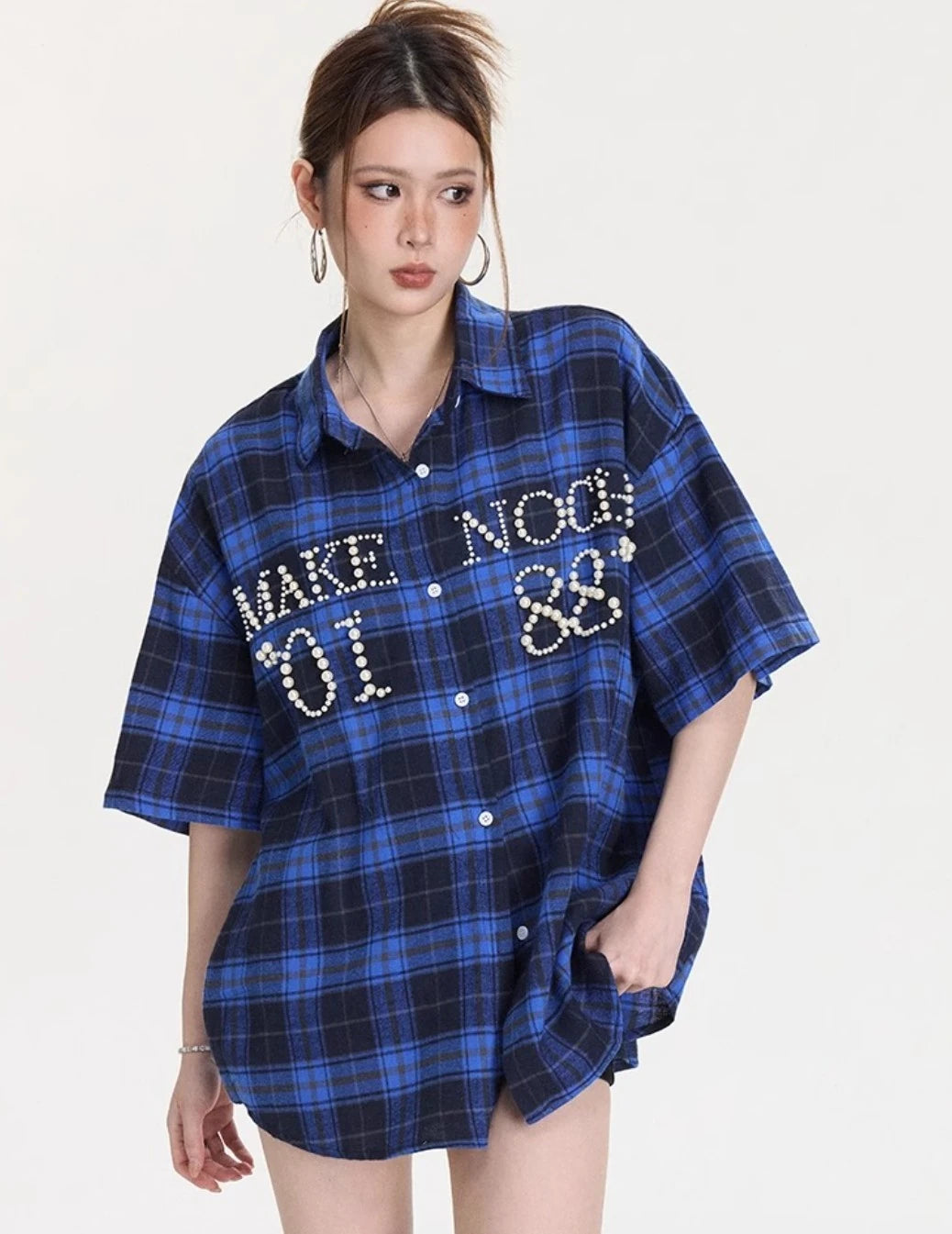 ブルー×ネイビーチェック柄のオーバーサイズシャツをブラックショートパンツとブルースニーカーに合わせた全身コーデ写真。フロントのパールレタリングが目立つスタイル。