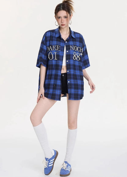 ホワイトのクロップドタンクの上に羽織ったブルー×ネイビーチェック柄オーバーサイズシャツの正面アップ。胸ポケットのパール装飾とリラックスした着こなしが特徴。