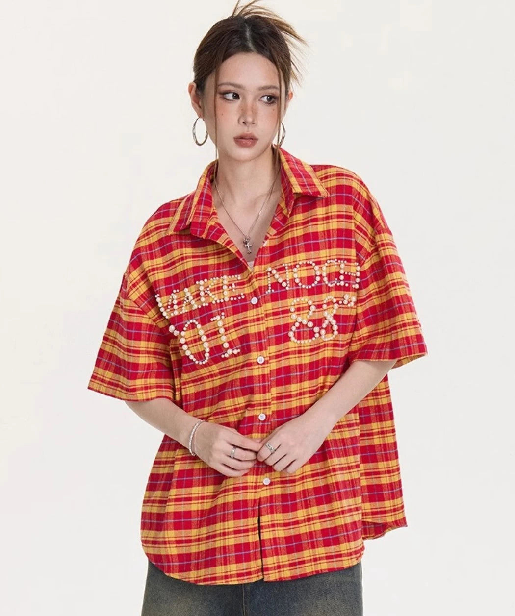 ボタンを留めた状態のイエロー×レッドチェック柄オーバーサイズシャツのフロントスタイリングカット。胸元のパール装飾が際立つデザイン。