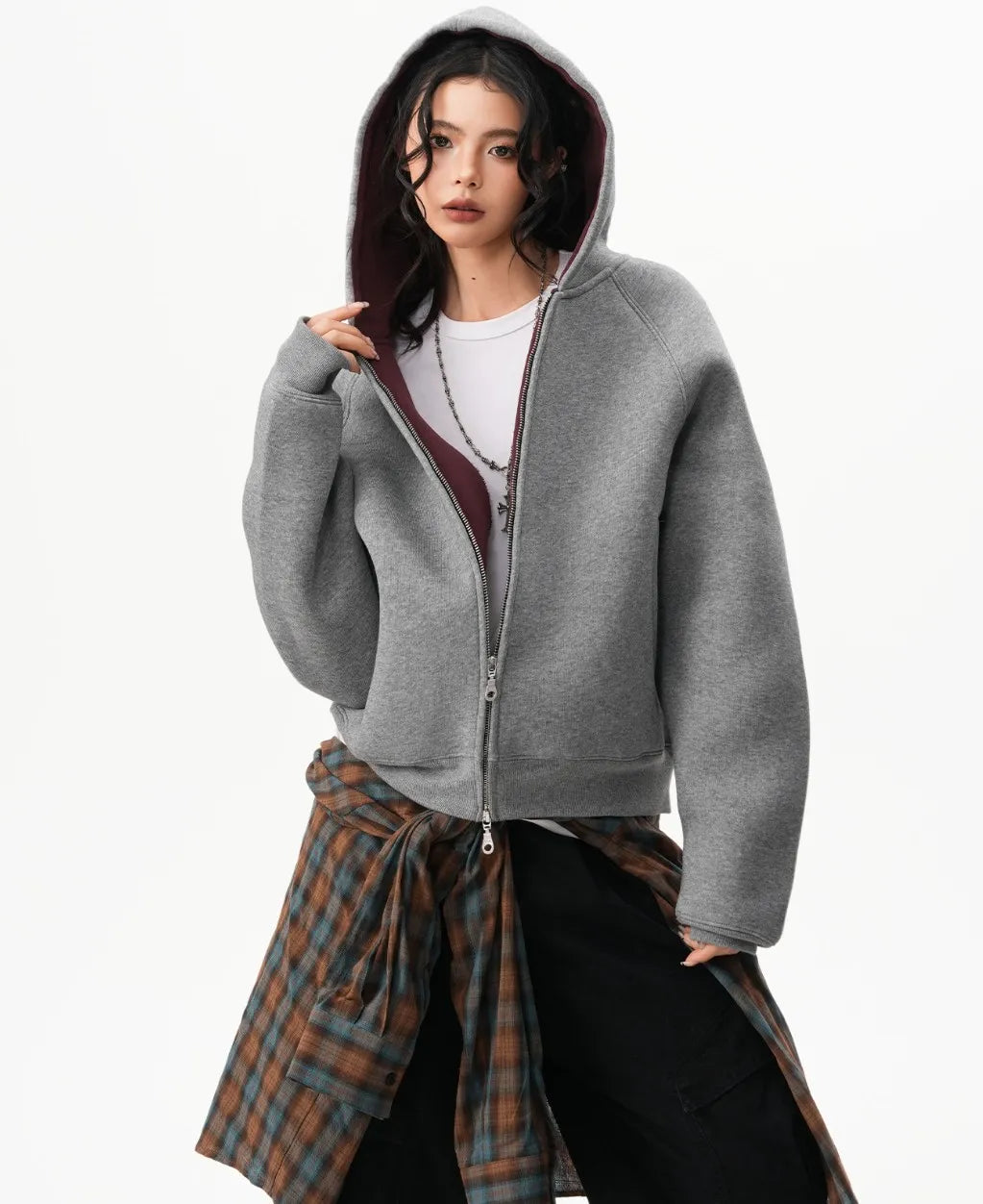 フードをかぶり前ジップを少し開けたグレーのラグランパーカーとチェックシャツコーデの写真