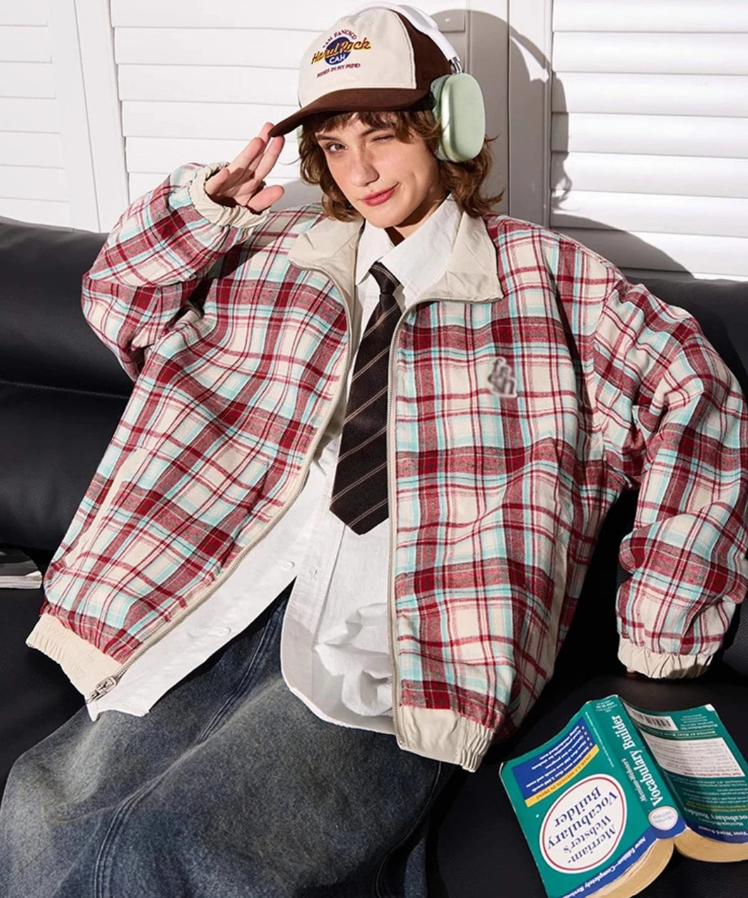 赤チェック柄側のリバーシブルジャケットを着たモデル。ソファで本を読む。