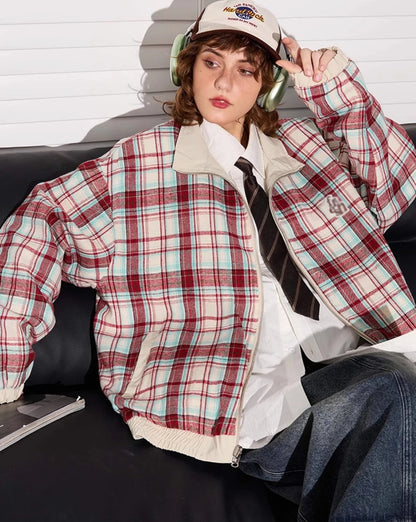 赤チェック柄側のリバーシブルジャケットを着たモデル。ソファに座り、キャップを触る。