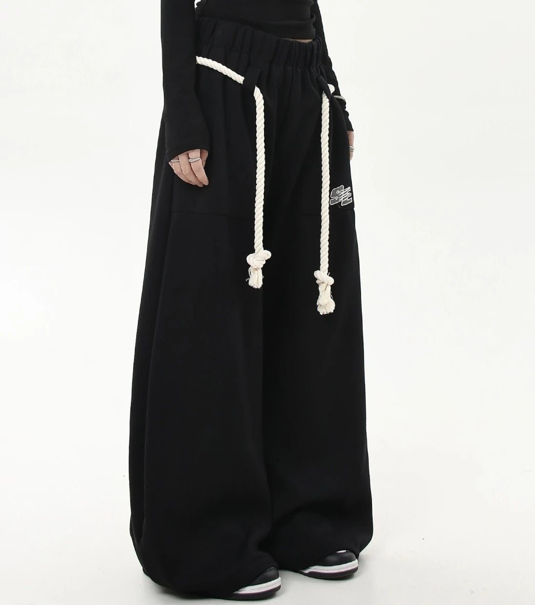 ロープベルトとロゴパッチが付いたブラックワイドスウェットパンツの斜めフロントショット。腰回りのディテールが分かりやすい。