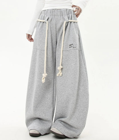 ウエストにホワイトロープベルトを巻いたグレーワイドスウェットパンツのバックショット。ヒップから裾までまっすぐ落ちるワイドシルエットが分かる。