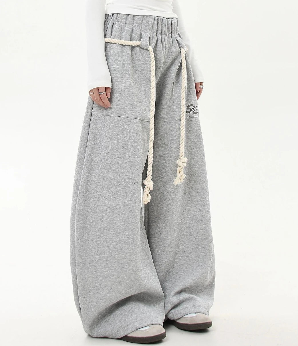 ロープベルトとロゴプリントが入ったグレーワイドスウェットパンツのアップ寄りフロント画像。ウエストギャザーやポケット位置のディテールが見える。